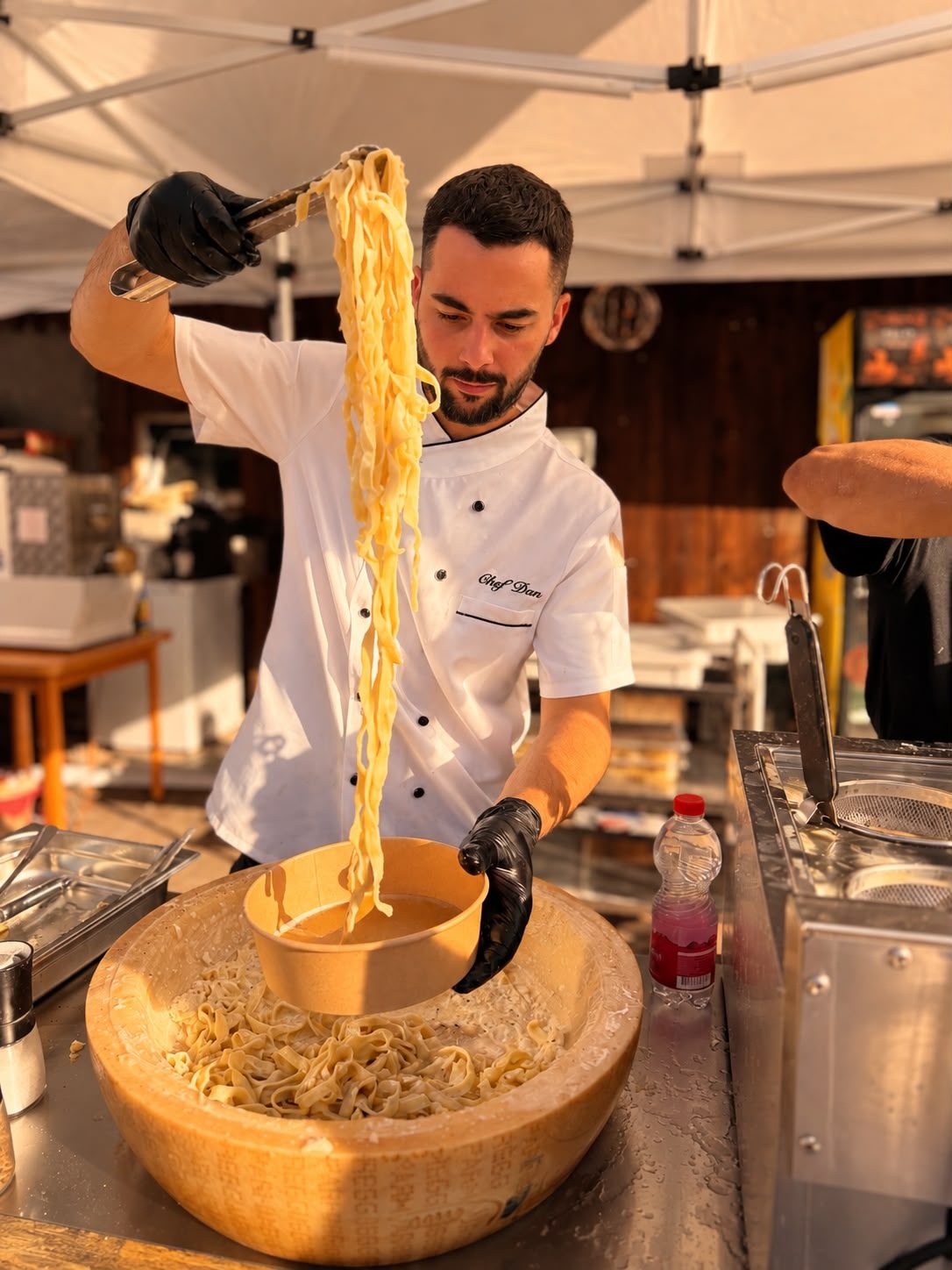 Chef Dan in weisser Jacke hebt Tagliatelle mit einer Zange in eine Schale.